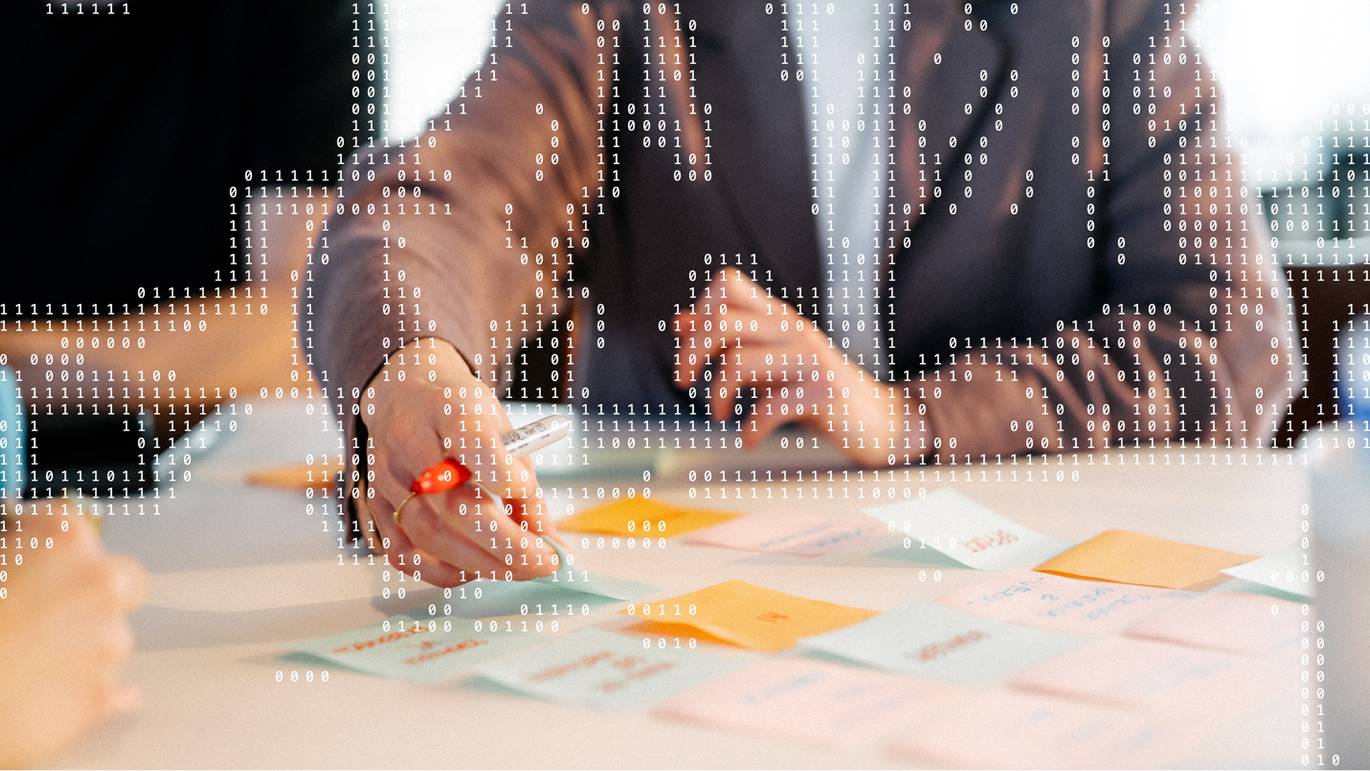 To personer arbejder med post-its på et bord. Binær kode er lagt hen over billedet som et grafisk element.